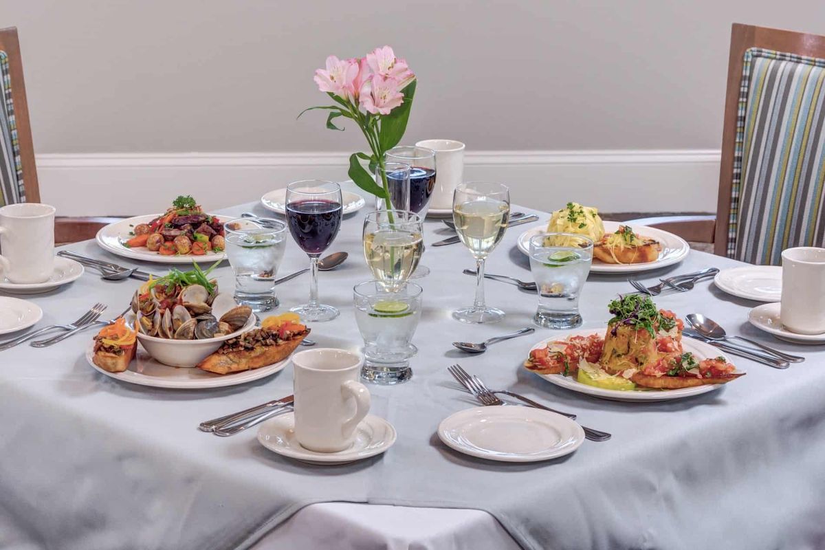 An elegantly set dining table with a flower centerpiece and various dishes accompanied by wine glasses.