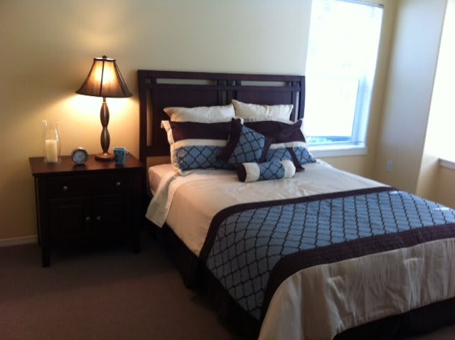 A neatly arranged bedroom featuring a bed with patterned pillows and a bedside lamp.
