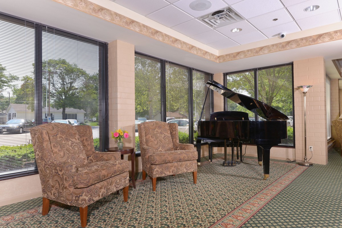 A cozy lobby area featuring a grand piano and two upholstered chairs by large windows.