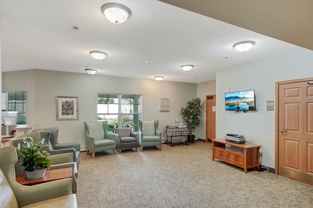 A cozy waiting room with comfortable chairs, a television, artwork on the walls, and soft lighting.