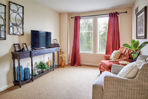 A cozy living room with a television, comfortable seating, and natural light streaming through the windows.