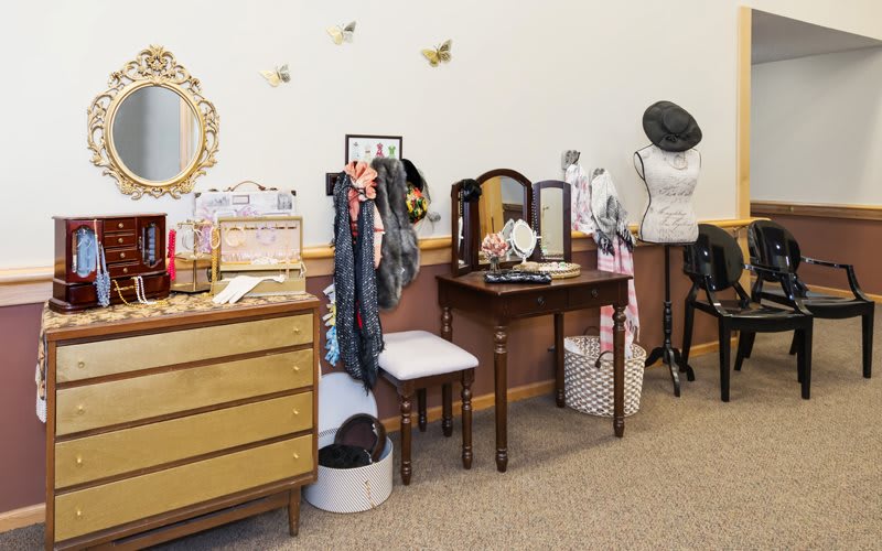 A vintage-themed dressing area featuring a vanity with a mirror, fashion accessories, and a hat stand.