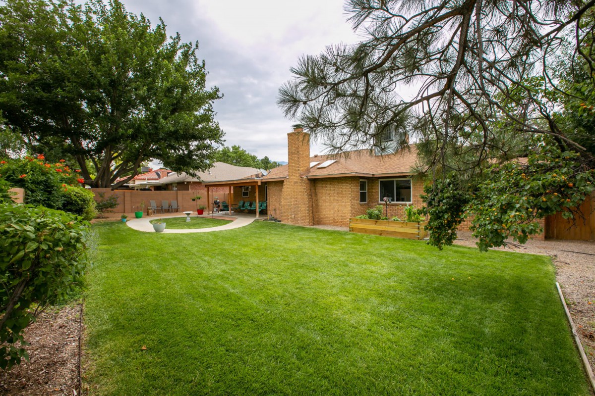 A suburban backyard featuring a well-maintained lawn, trees, and a brick house with a chimney.