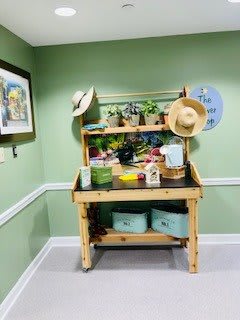 A cozy indoor gardening setup with a wooden table, potted plants, and decorative hats against green walls.