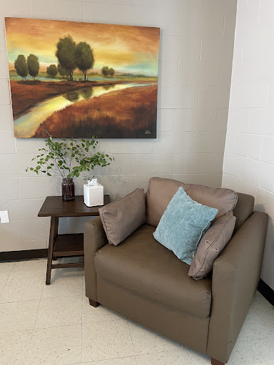 A cozy corner featuring a comfortable armchair, decorative cushions, and a serene landscape painting.