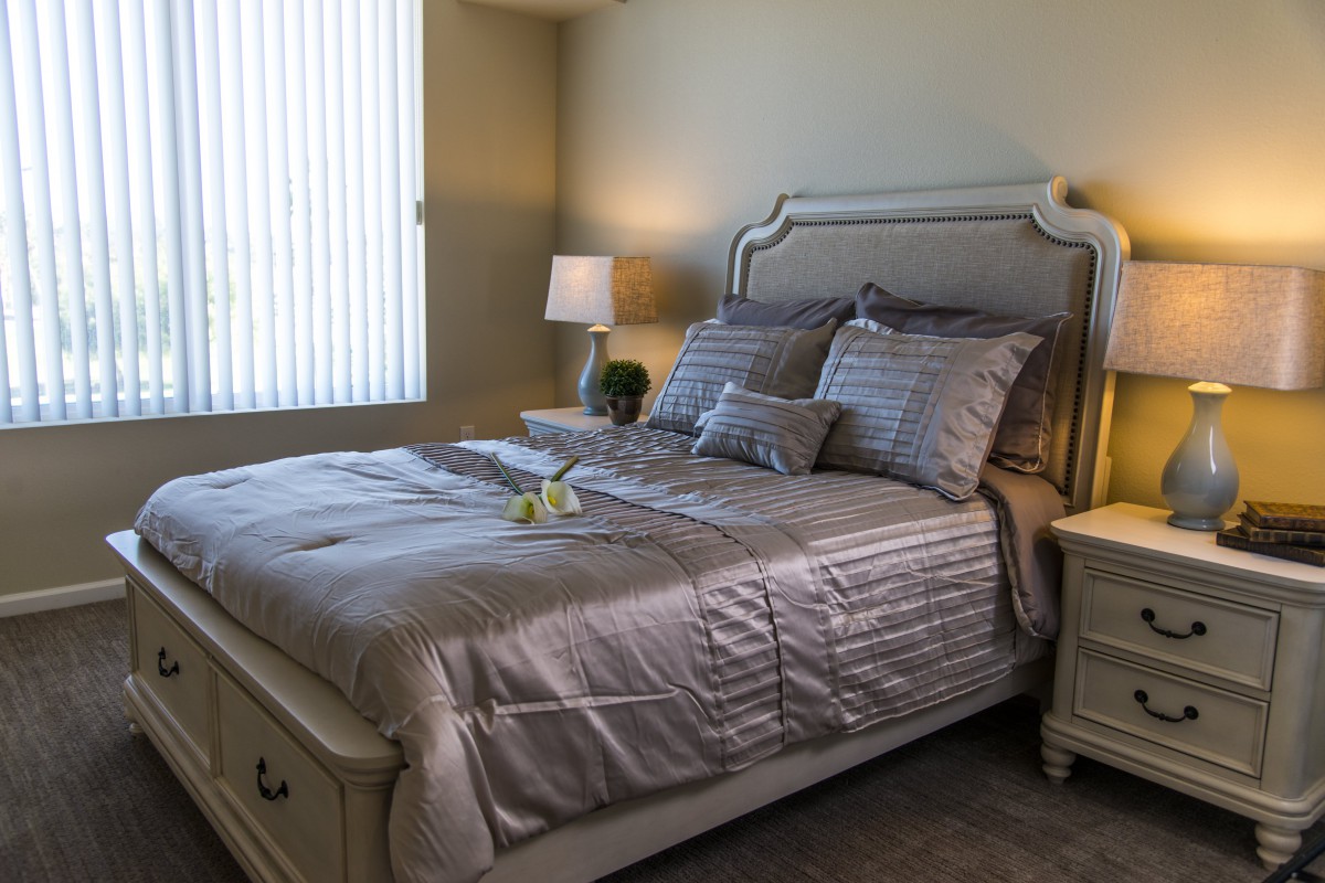 A well-appointed bedroom with a stylish bed set, including silky gray bedding, matching pillows, and a nightstand with a lamp.