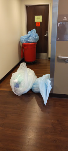 Two bags of waste positioned near a door in a hallway with a red trash bin in the background.