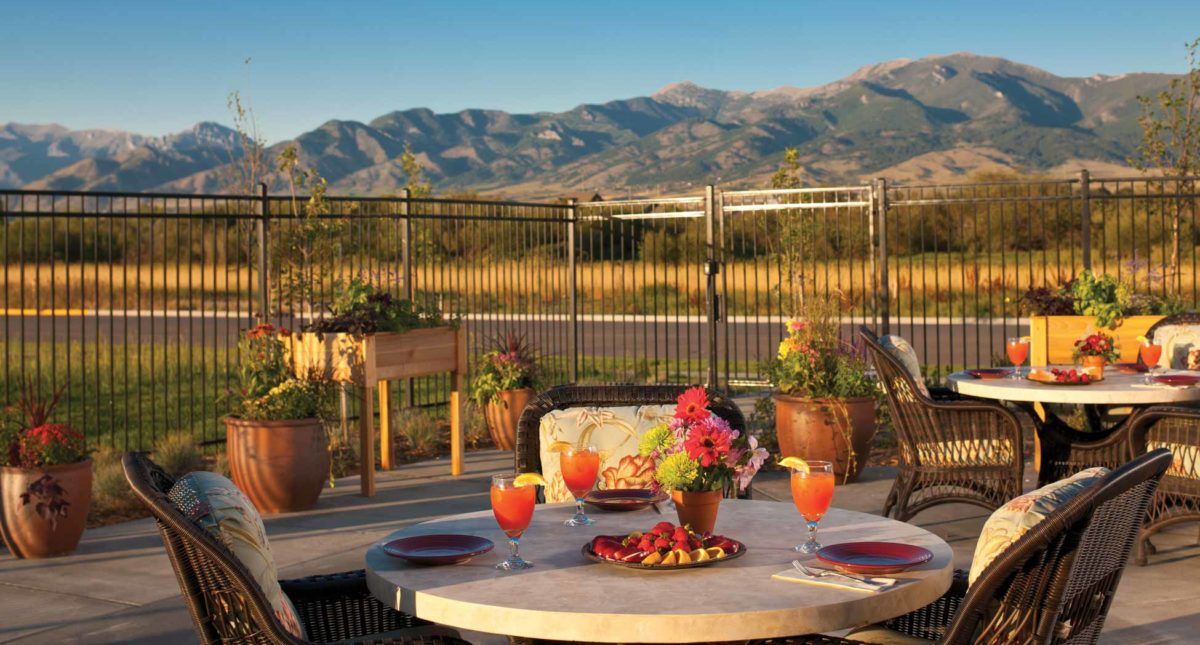A scenic outdoor patio with a view of mountains, featuring a nicely set table with drinks and flowers.