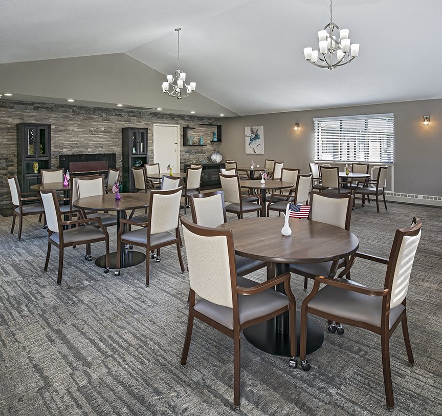 A spacious dining room with multiple tables and chairs, featuring elegant chandeliers and a carpeted floor.