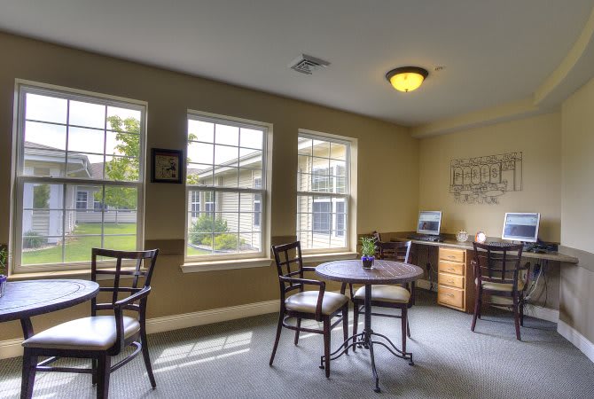 A cozy room with tables, chairs, and ample natural light from large windows.