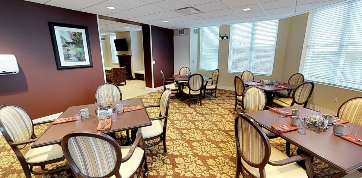 A cozy dining area with elegant tables and chairs, featuring a patterned carpet and large windows.