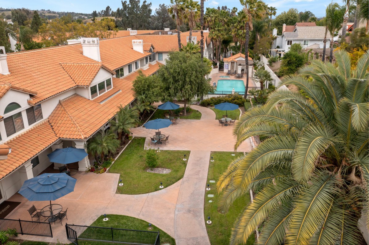 An aerial view of a hotel courtyard with pathways, palm trees, and a swimming pool.