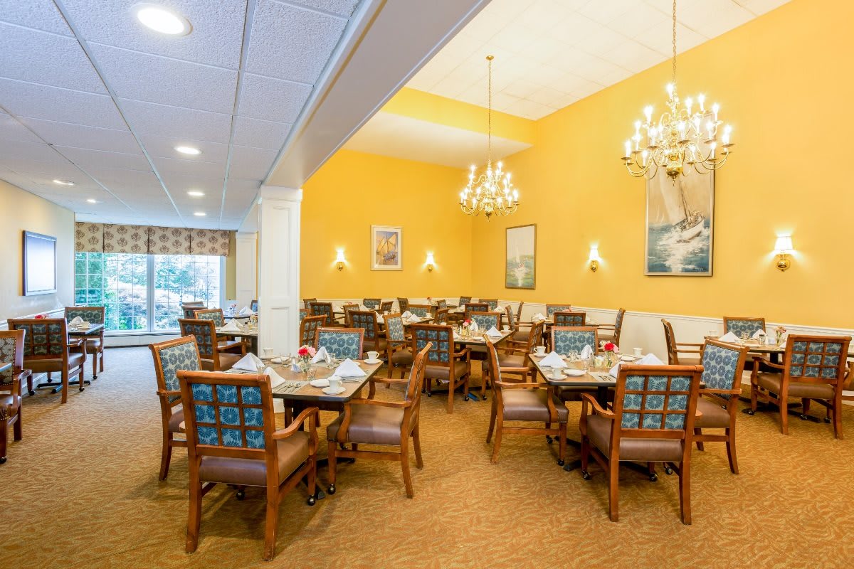 A well-lit dining room with elegant chandeliers and neatly arranged tables and chairs.