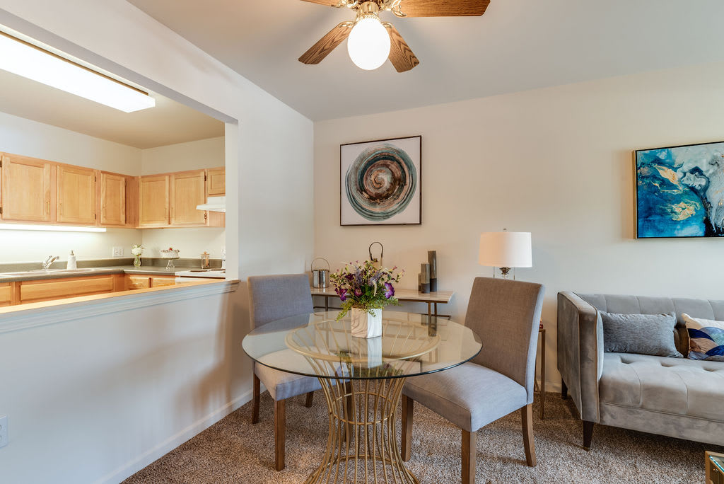 A cozy dining area with a glass table, surrounded by chairs, and decorated with artwork and a lamp.