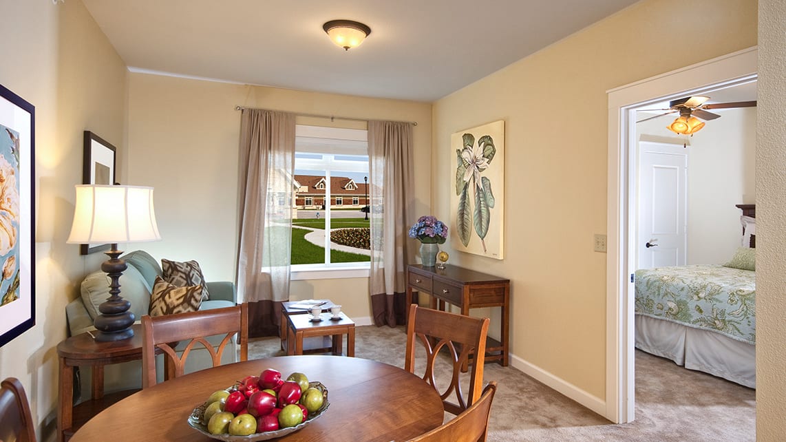 A cozy living room with a dining area featuring elegant furniture, artwork on the wall, and a window offering a scenic view.