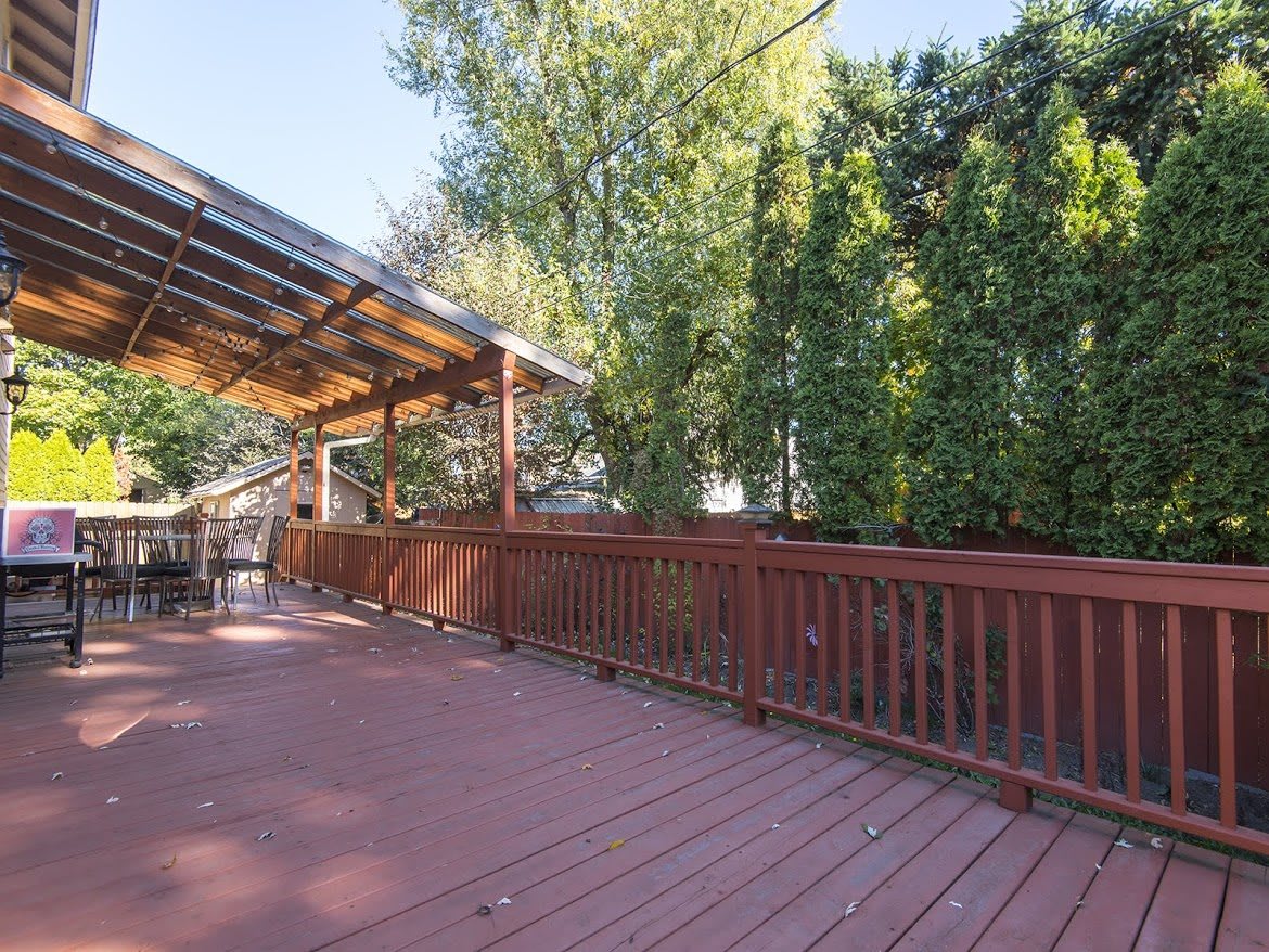 A spacious wooden deck with a covered area, surrounded by trees and a fence.