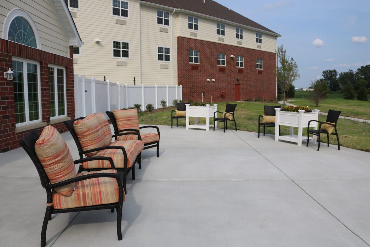 An outdoor patio area with chairs and a view of a brick building and fence.