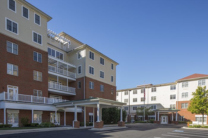 A modern residential apartment complex with multiple stories and a covered entrance, set against a clear blue sky.