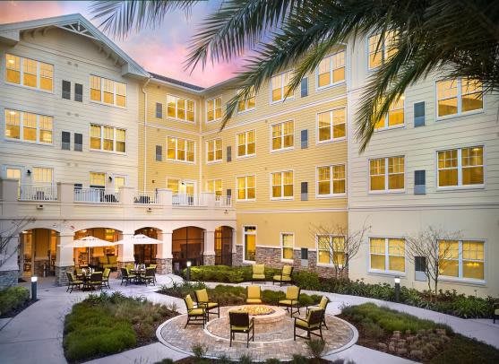 A residential building with a courtyard featuring outdoor seating and surrounded by palm trees during the evening.