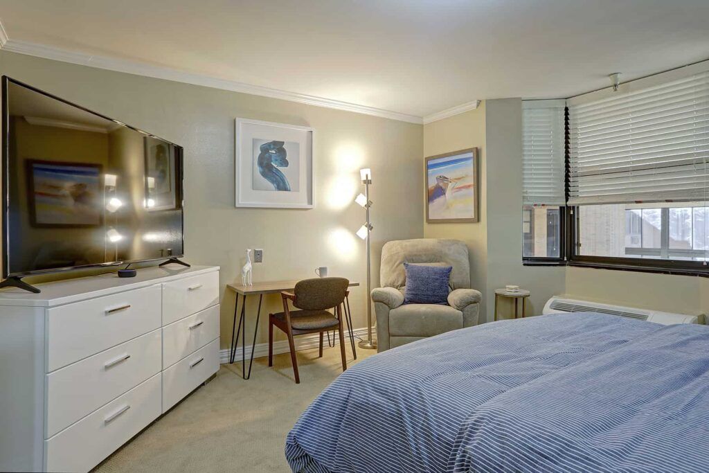A cozy bedroom with modern decor, featuring a bed, dresser, artwork, and a comfortable chair.
