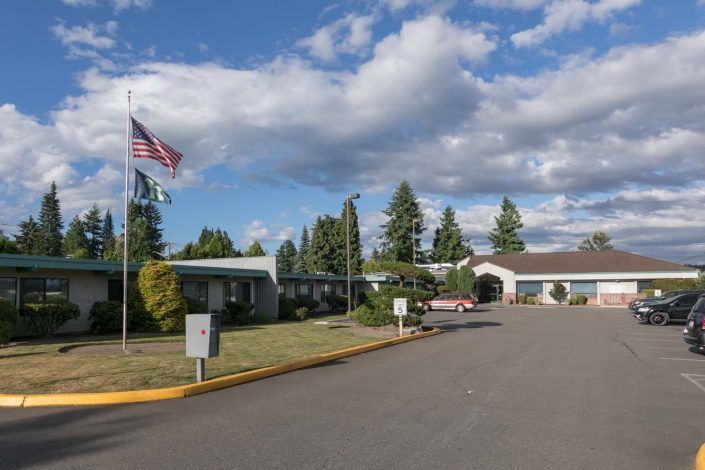 A building with flags and a driveway surrounded by trees under a cloudy sky.