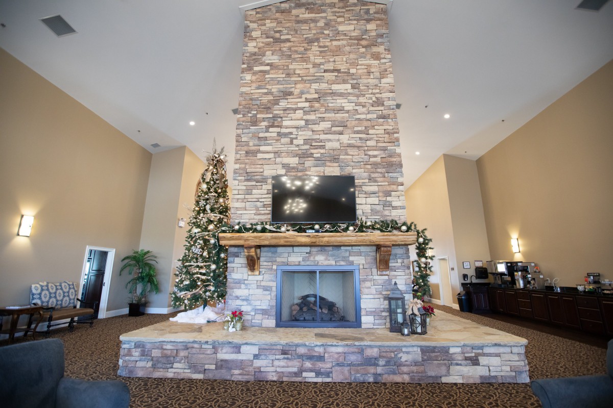 A festive living room featuring a tall stone chimney with a TV mounted above the fireplace, adorned with holiday decorations and a beautifully decorated Christmas tree.