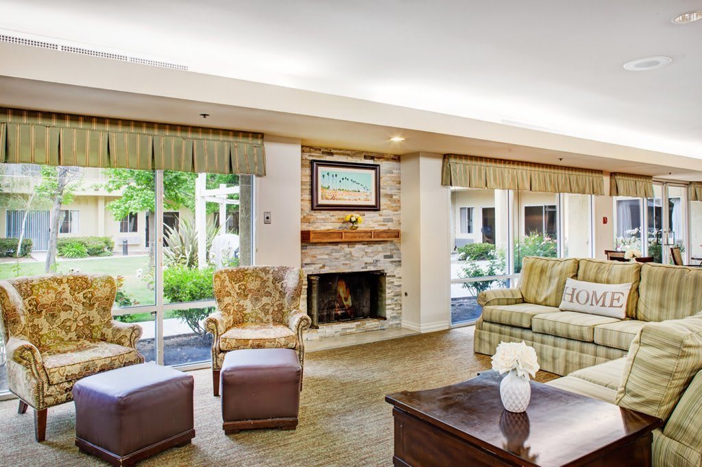A cozy living room with a fireplace, comfortable seating, and large windows overlooking a garden.