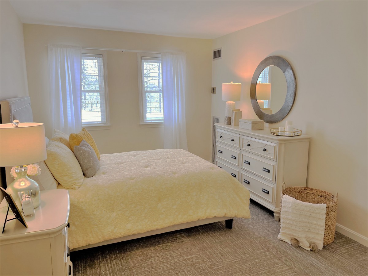 A cozy bedroom with neutral tones, featuring a bed, dresser, and large mirror.