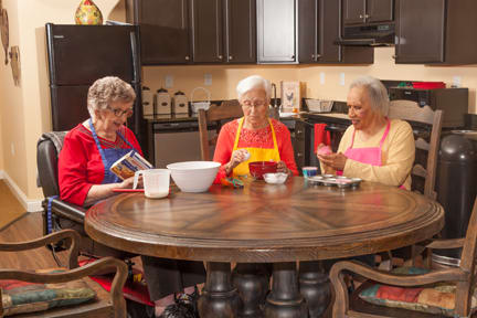 Three elderly women sitting around a table in the kitchen, preparing food together.