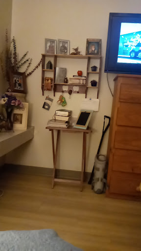 A cozy corner featuring a wooden shelf with various decorations, books, and a tablet on a small table.