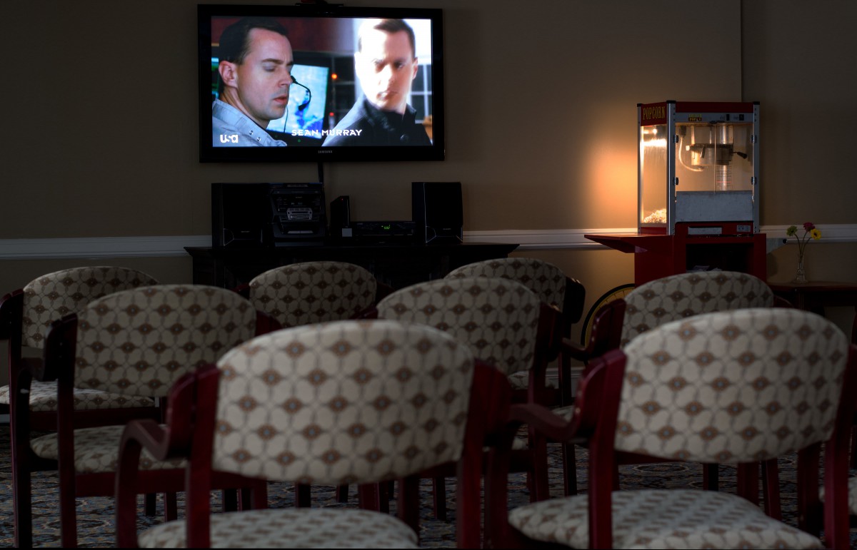An empty room with patterned chairs facing a television screen playing a movie, accompanied by a popcorn machine in dim lighting.
