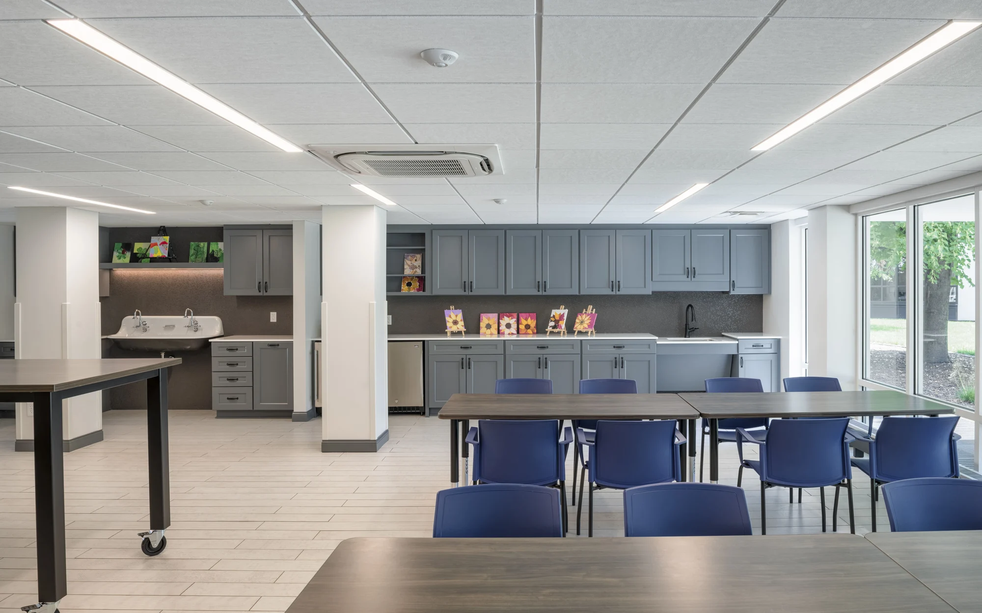 A modern office kitchen with blue chairs and spacious gray cabinets.