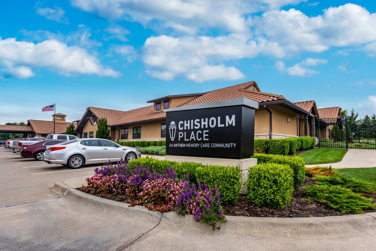 A healthcare facility named Chisholm Place, featuring well-maintained landscaping and a clear sky overhead.