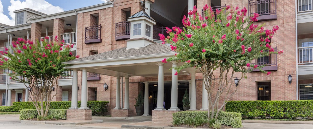 A building entrance with columns and a flowering tree nearby.