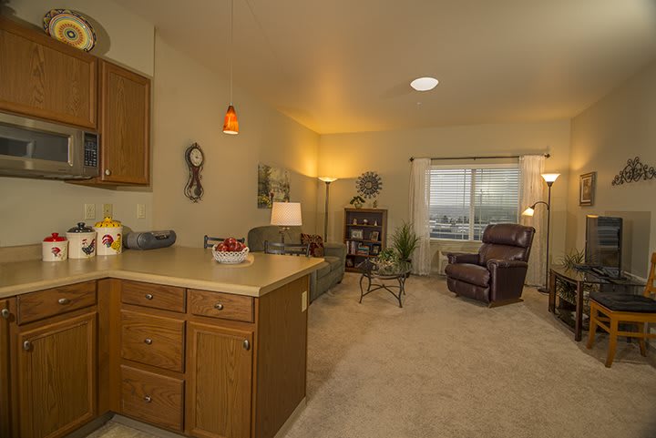 A cozy living room with a view of the kitchen area, featuring comfortable seating and warm lighting.