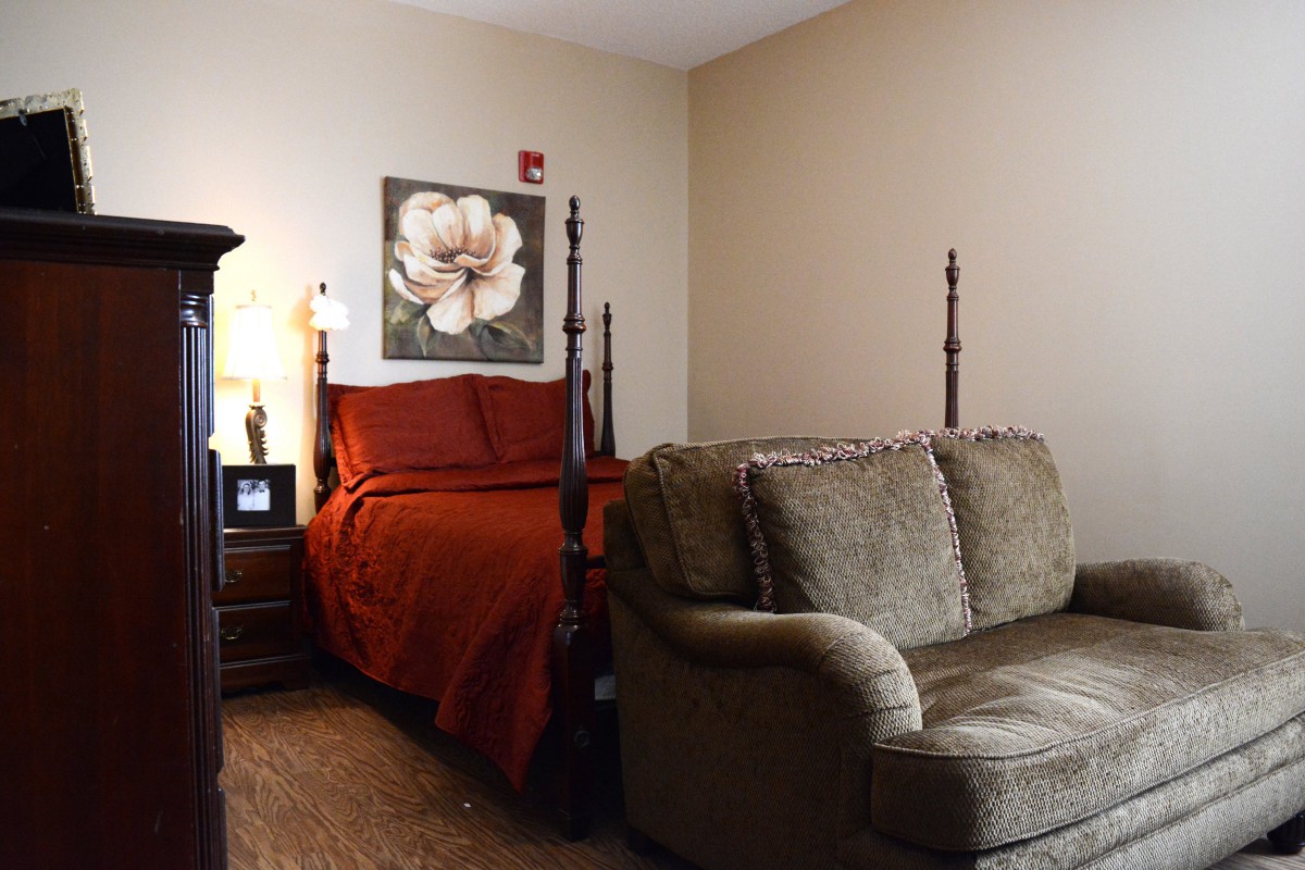 A cozy bedroom with a four-poster bed, a sofa, and a floral painting on the wall.