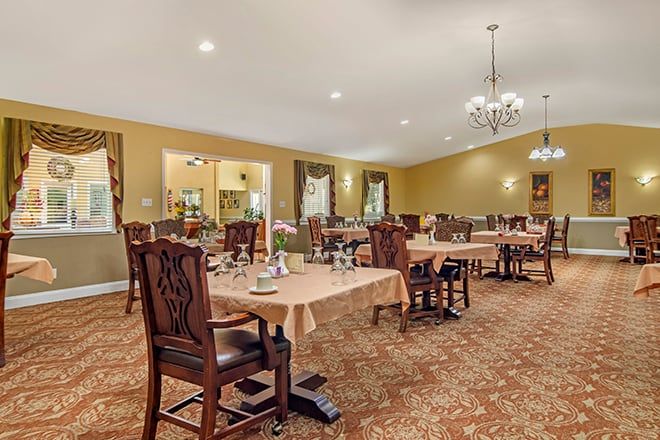A well-decorated dining room with several tables and chairs, illuminated by chandeliers.