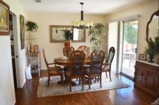 A warm and inviting dining room featuring a wooden table set with matching chairs, complemented by a patterned rug and lush plants. Natural light pours in through the sliding glass door, highlighting the elegant decor.