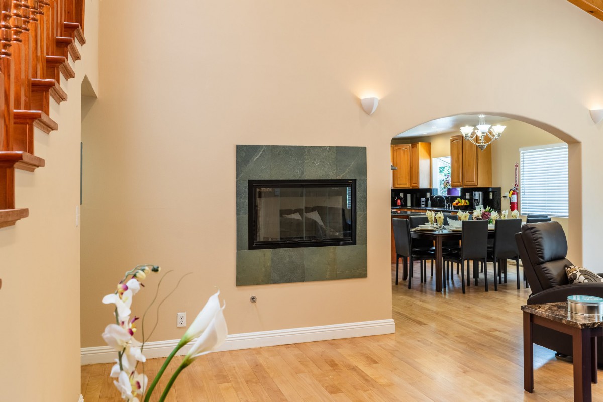 A modern open-concept living space featuring a sleek fireplace, wood flooring, and a glimpse into the dining area.