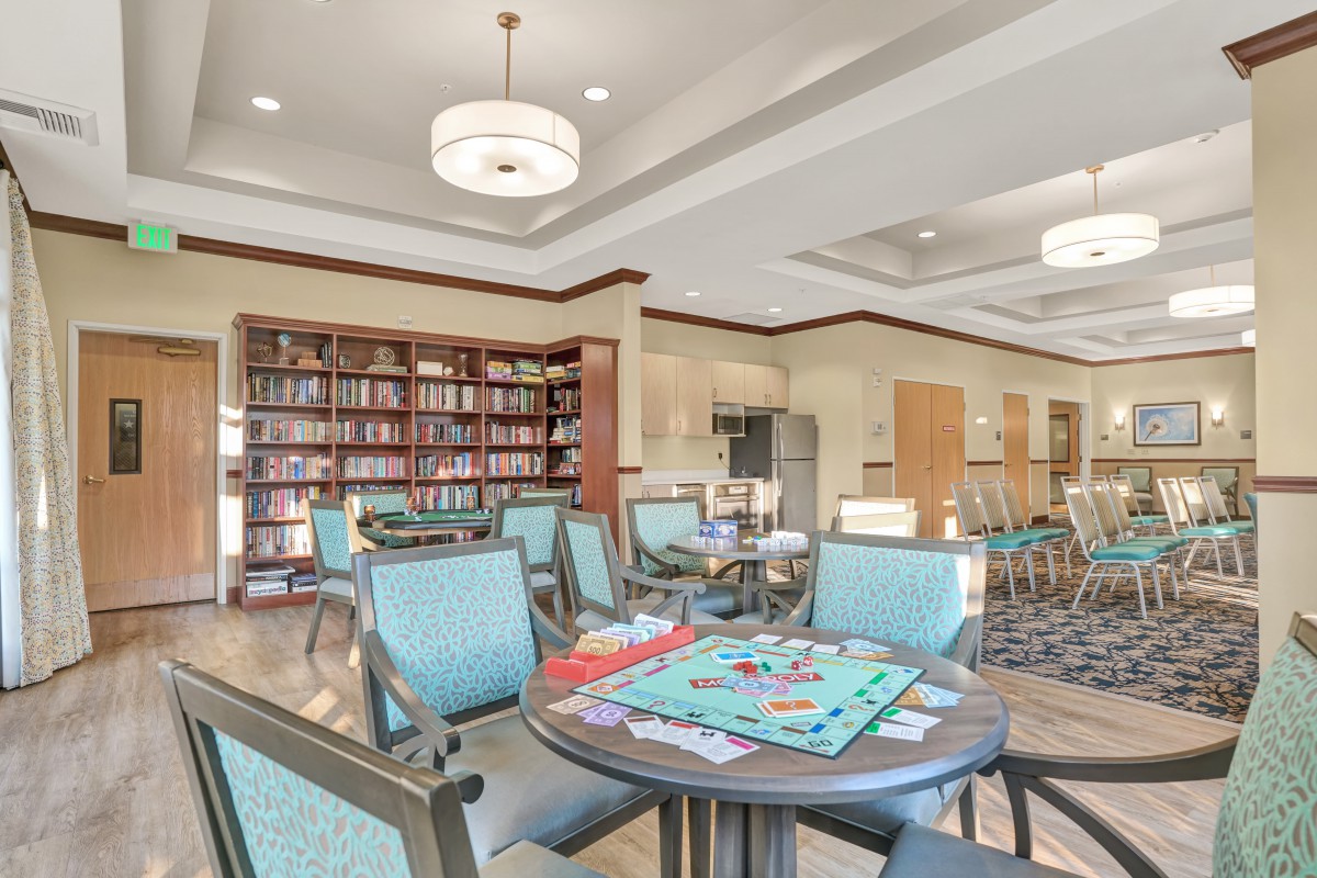 A cozy community library area with tables set up for board games and bookshelves lining the walls.