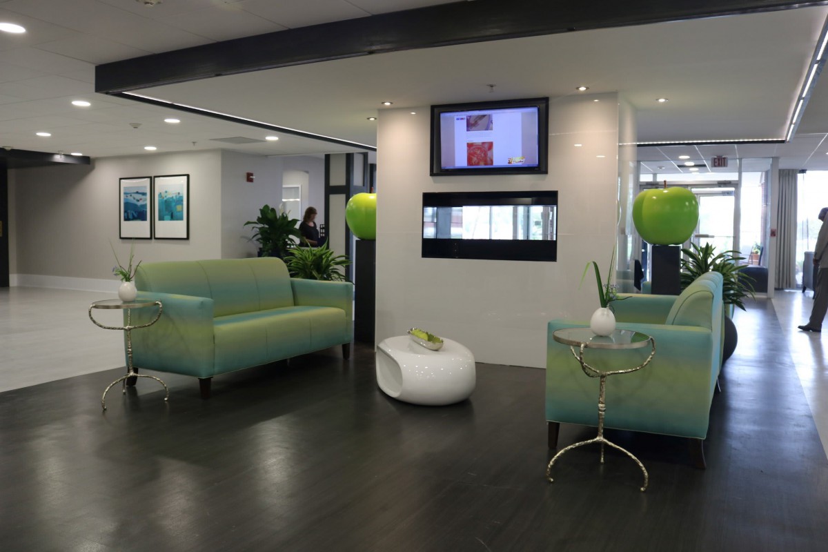 A modern lobby with green couches and decorative plants, featuring a wall-mounted television.