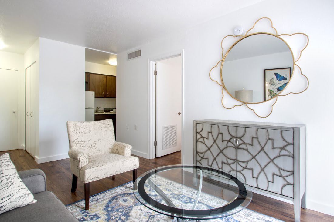 A modern living room with a patterned chair, glass coffee table, and decorative mirror.