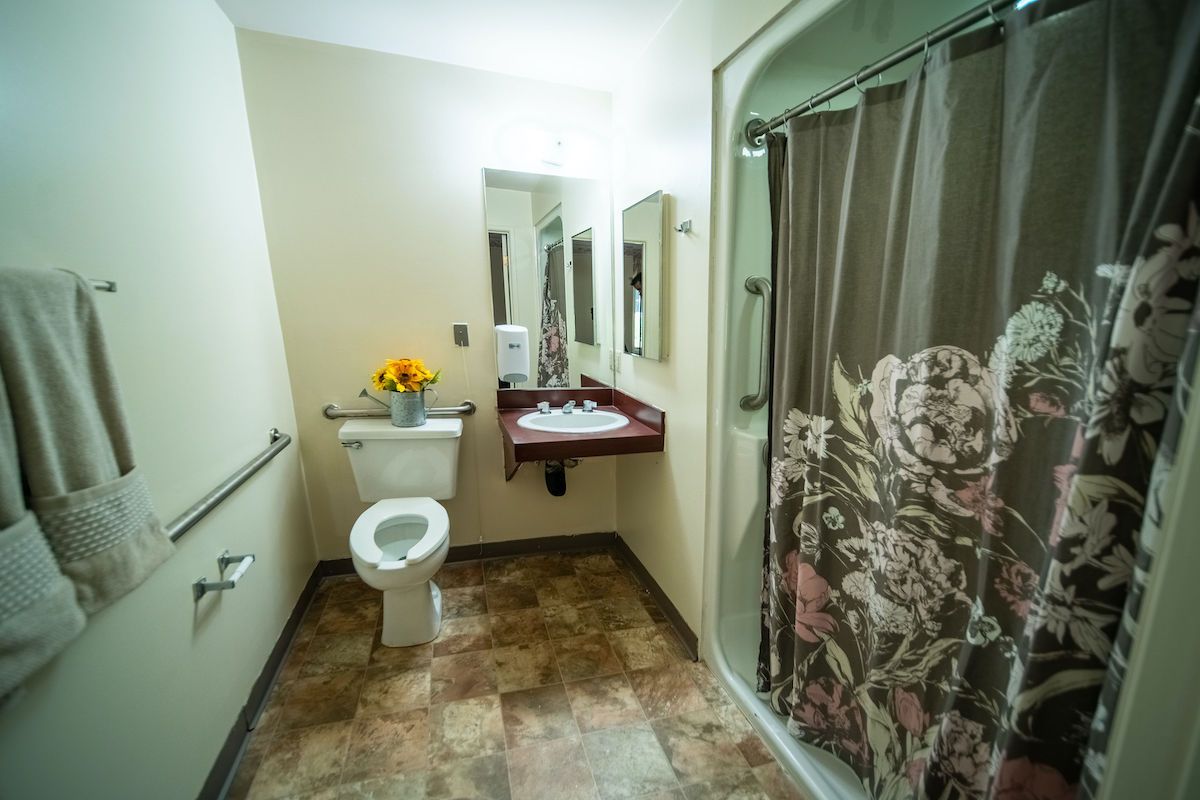 A bathroom with a toilet, sink, shower, and floral decoration.