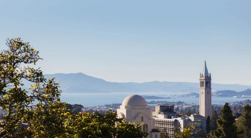 A scenic view of a city with a prominent dome-shaped building, overlooking the ocean and distant mountains.