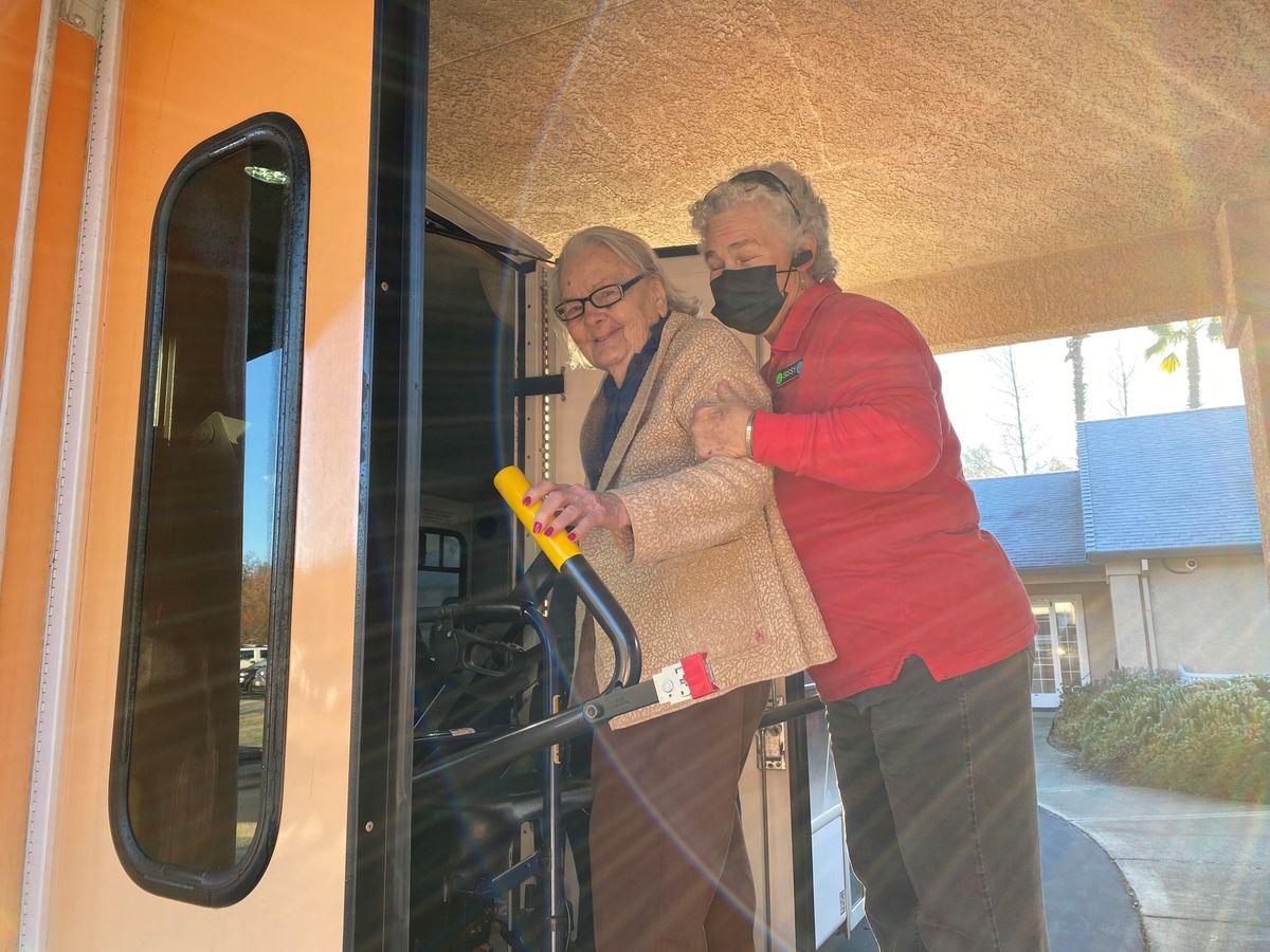 Two elderly individuals navigating a bus, with one providing support to the other.