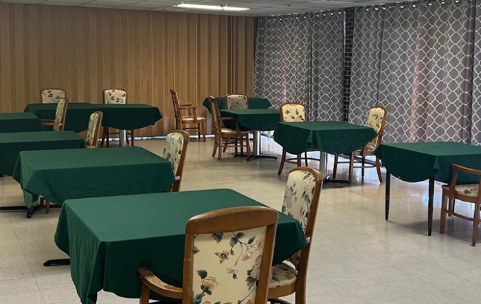 A dining room with several tables covered in green tablecloths and floral-patterned chairs, set against a backdrop of curtains.