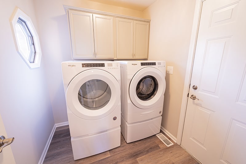 A laundry room featuring a front-loading washer and dryer set beneath overhead cabinets.