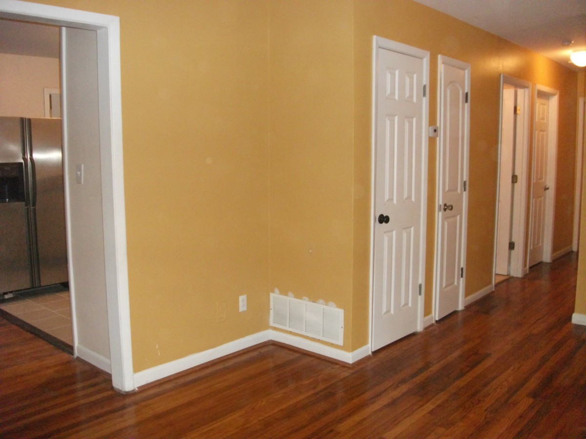 A hallway with yellow walls, wood flooring, and several white doors.