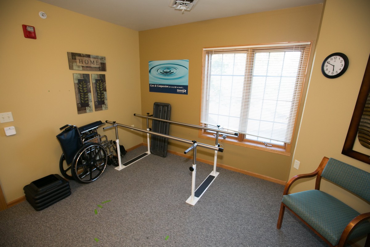 A rehabilitation room equipped with parallel bars and a wheelchair next to a window.