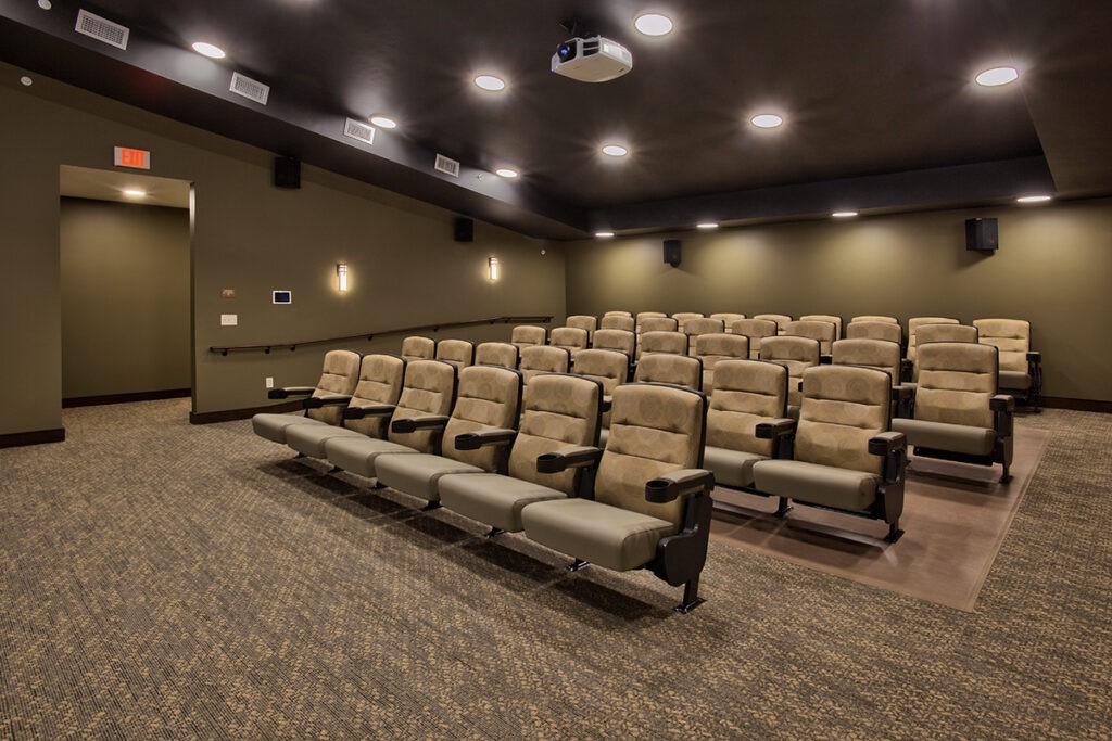 An empty theater room with rows of seats and a ceiling-mounted projector.